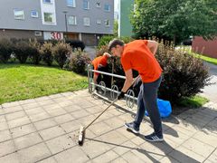 En ungdom i orange t-shirt sopar stenläggningen framför ett hus.