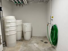Stora vita plasthinkar står på ett betong golv, en grön vattenslang hänger på väggen.