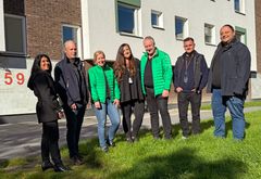 Sju personer står på en gräsmatta framför ett flerbostadshus.