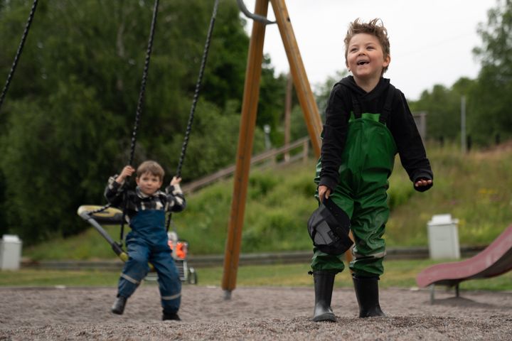 Två glada barn gungar i en lekpark i Botkyrka.