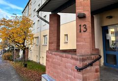 Entrén till ett flerbostadshus. I bakgrunden ett träd med höstlöv.