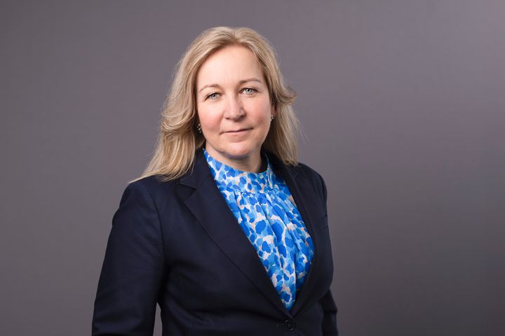 En blond kvinna i svart kavaj och blåmönstrad blus.