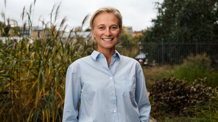 En leende kvinna med kort blont hår i ljusblå skjorta