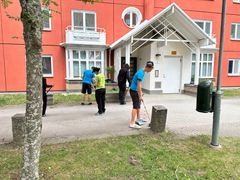 Unga personer städar utomhus framför hus i orange och vitt.