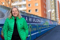Kvinna i grön jacka framför målad mur och bostadshus