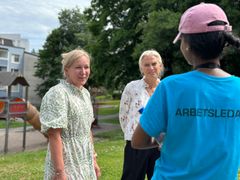 Två blonda kvinnor i somriga kläder står och pratar med en person i blå t-shirt med ryggen vänd mot kameran.