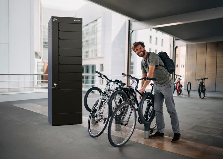 Man låser fast sin cykel vid ett cykelställ intill ett svart laddskåp från Eco Charge i en modern urban miljö