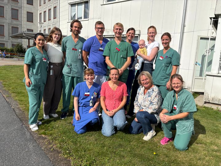 Ett 10-tal vårdpersonal står samlade utomhus med sjukhuset i bakgrunden. De flesta är vårdklädda i grönt eller blått.