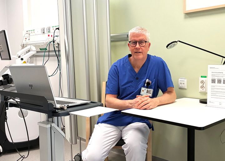 Ett porträtt av en man i sjukhuskläder som sitter vid sitt skrivbord.