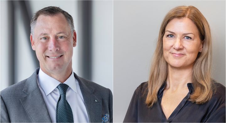 Två personer, en man och en kvinna, i formella kläder står och ler mot kameran.