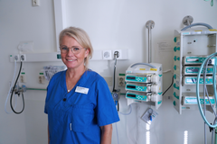 En kvinna iklädd sjukvårdskläder står riktad mot kameran och ser glad ut.