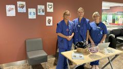 Tre vårdpersonal i blå kläder står vid ett informationsbord om donation.