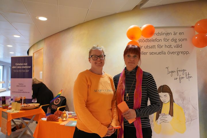 Två kvinnor som bär oranget och ler mot kameran.