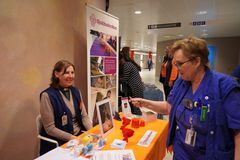 En kvinna från sjukhuskyrkan sitter ner vid sin monter och pratar med en sjuksköterska som går förbi.