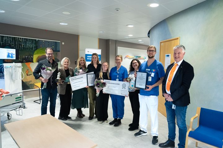 En grupp människor står i ett sjukhus och håller diplom och blommor.