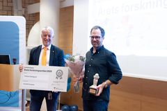 Tobias Dahlgren tar emot priset för Årets forskningsartikel 2023, står med en utmärkelse och blommor tillsammans med en sjukhusdirektör.