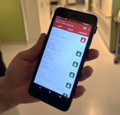 En hand håller en smartphone som visar ett larmsystem för vårdpersonal.