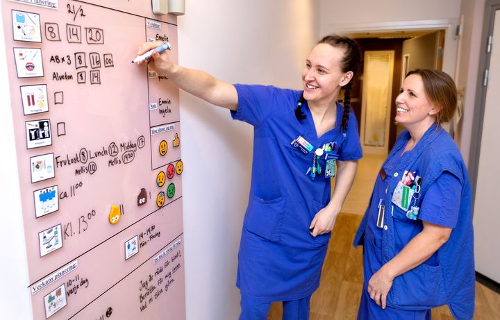 Barnsjuksköterskan Emelie Bergh och specialistundersköterskan Evelina Grünert framför glastavlan i ett av patientrummen.