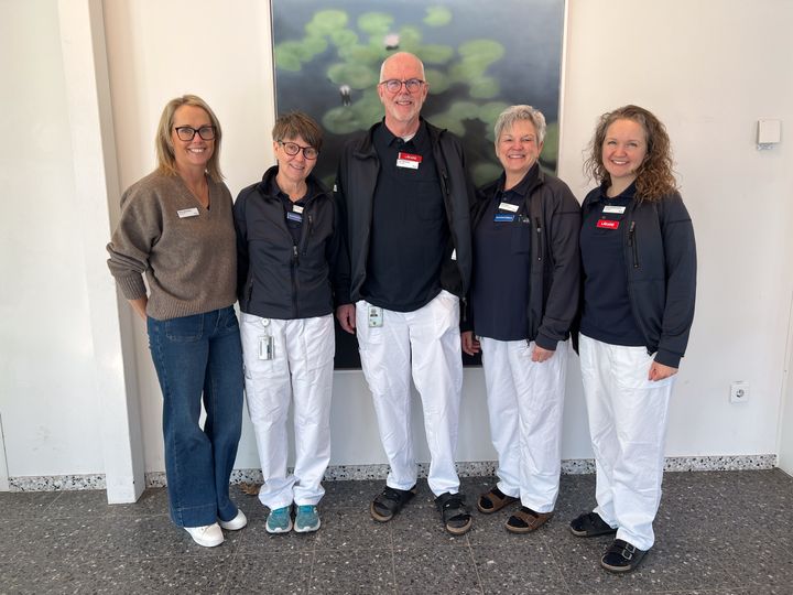 Fyra sjukvårdspersonal och en enhetschef står framför en vägg. De är klädda i arbetskläder och ler mot kameran.