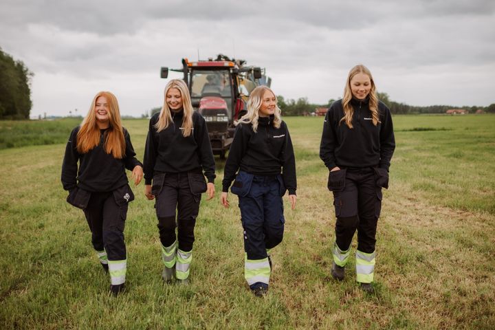 Fyra elever i arbetskläder går på en åker med en traktor i bakgrunden.