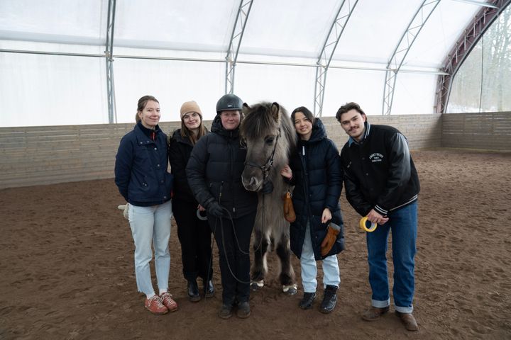 En grupp studenter från Chalmers står med en islandshäst och Malin Jansson från Axevalla Hästcentrum inomhus i ett ridhus.