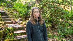 Person i en trädgårdsmiljö med grönska och stentrappa i bakgrunden.