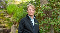 En person står utomhus i en trädgård, omgiven av grönska.