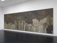 Stor abstrakt målning i mörka grå och beige toner på vit vägg ovanför mörkt golv i utställningsrum.