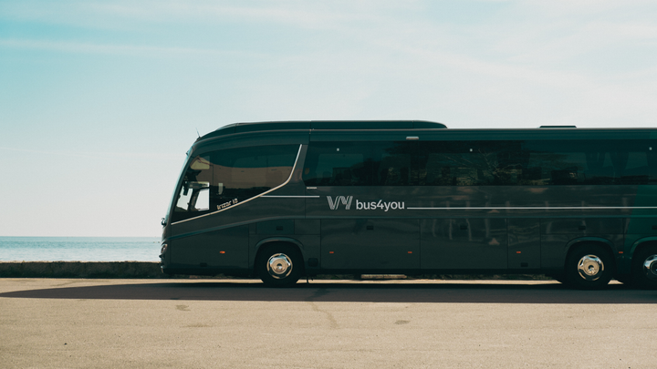 En svart Vy bus4you-buss står parkerad vid en väg med havet i bakgrunden.