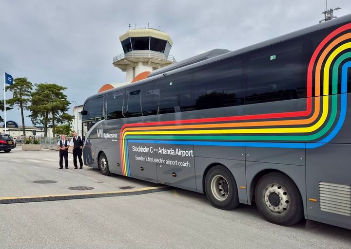 En eldriven flygbuss från Vy på en parkeringsplats i Visby. Flygplatstornet syns i bakgrunden.