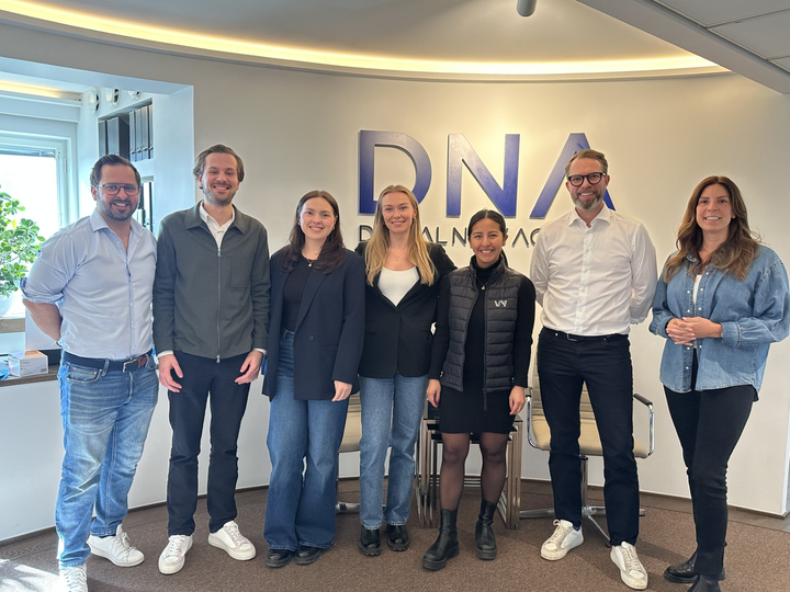 En grupp människor står framför en vägg med texten "DNA". Tre personer från Vy och fyra från DNA står tillsammans.