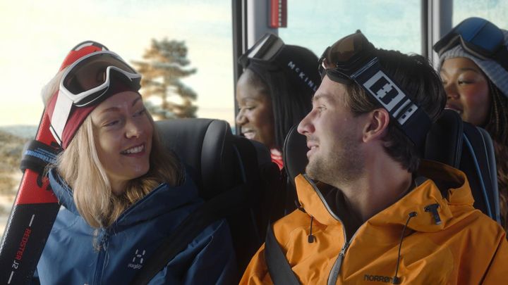 Fyra personer i skidkläder och skidglasögon sitter på en buss och ser glada ut.