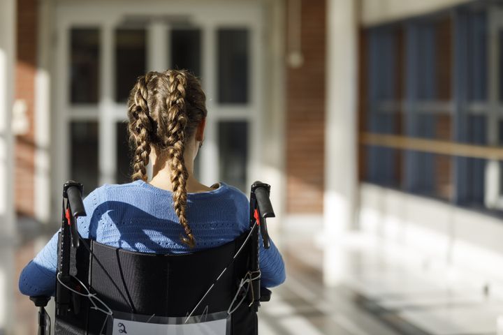 Kvinna i rullstol bakifrån vid ingång till byggnad