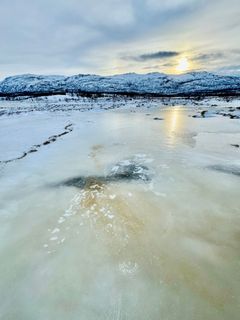 En snötäckt landskap med fjäll i bakgrunden. Vattendrag färgade roströda syns i förgrunden.