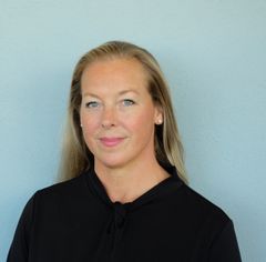 Kvinna med långt blont hår står framför en grå bakgrund