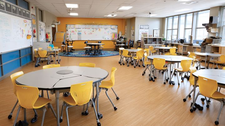 Alt text: Tomt klassrum med runda bord och gula stolar.