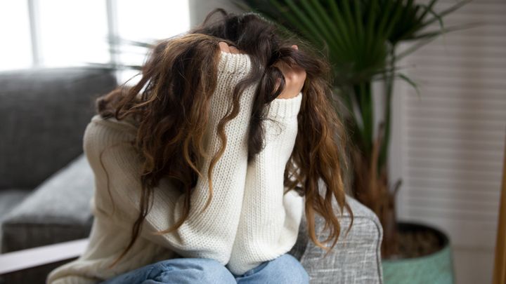 En person sitter med ansiktet dolt i händerna, iklädd en vit tröja.