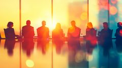 En grupp människor sitter vid ett konferensbord i ett modernt kontor, med ett stort fönster och soligt ljus i bakgrunden.