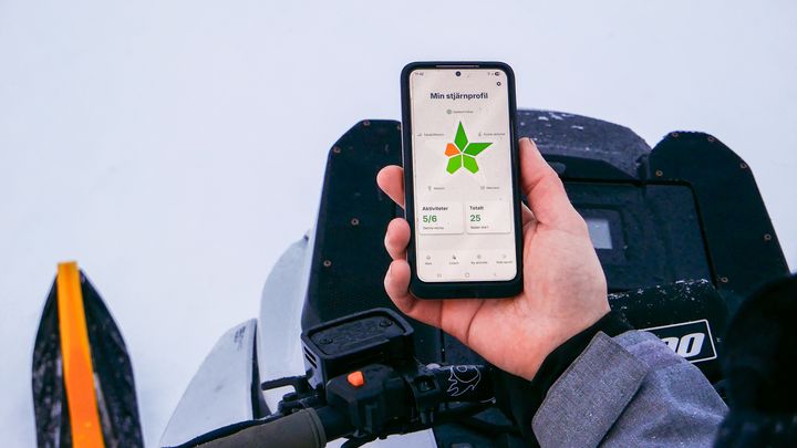 Person på snöskoter håller mobiltelefon med app i handen