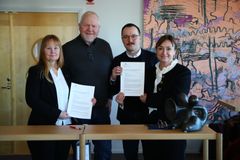 Personer står vid ett bord och håller upp dokument i en officiell miljö.