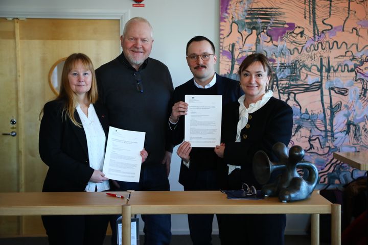 Personer står vid ett bord och håller upp dokument i en officiell miljö.