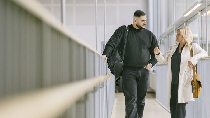 Två personer som står och pratar inomhus i en korridor.