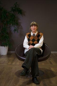 Bild på person sittande i en stol, med en växt i bakgrunden.