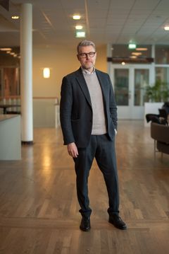 En man i kostym står i en ljus inomhusmiljö.