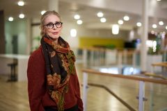 Kvinna med glasögon och halsduk i en ljus inomhusmiljö.