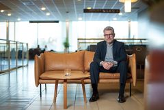 En man i kostym sitter på en brun soffa i ett modernt rum.