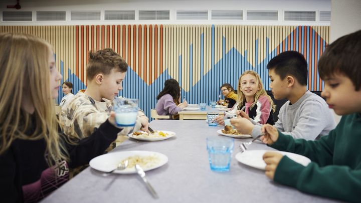 Elever sitter vid ett bord i en skolrestaurang och äter tillsammans.