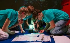 Bild på tre elever hukade över en tävlingsuppgift under Teknikåttans riksfinal