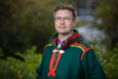 Forskaren Jon Petter Stoor i traditionell samisk dräkt står utomhus med grönska i bakgrunden.