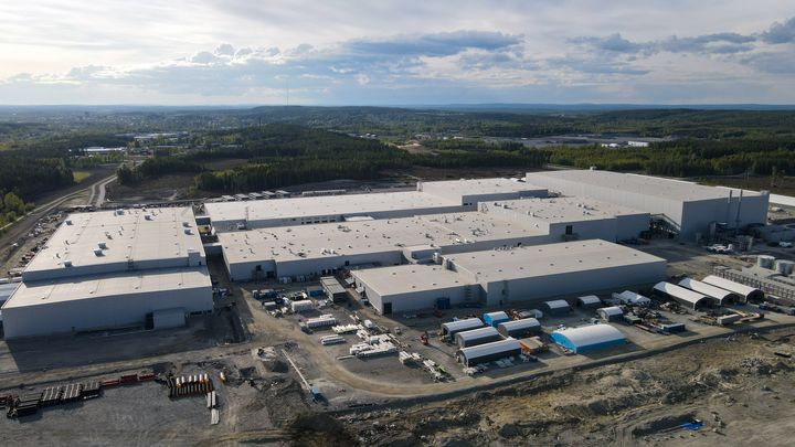 Flygbild av en stor industribyggnad omgiven av skog och vägar.